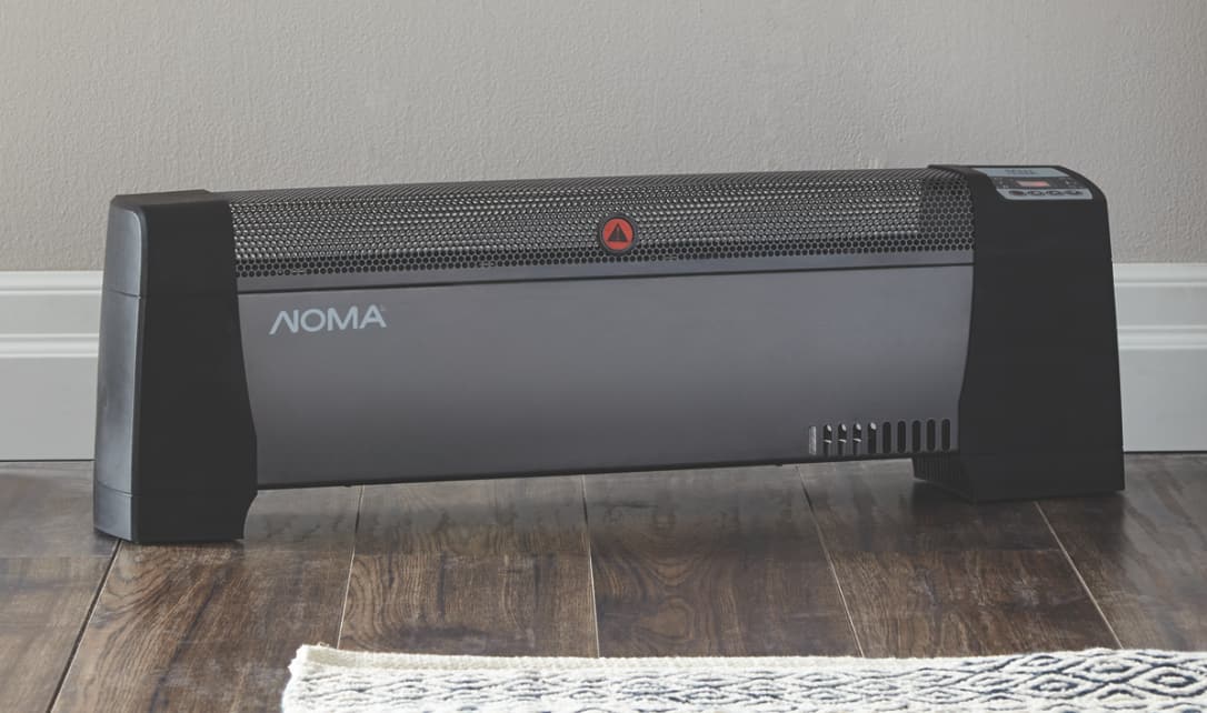 A Noma Digital Baseboard Heater on the floor of a bedroom.