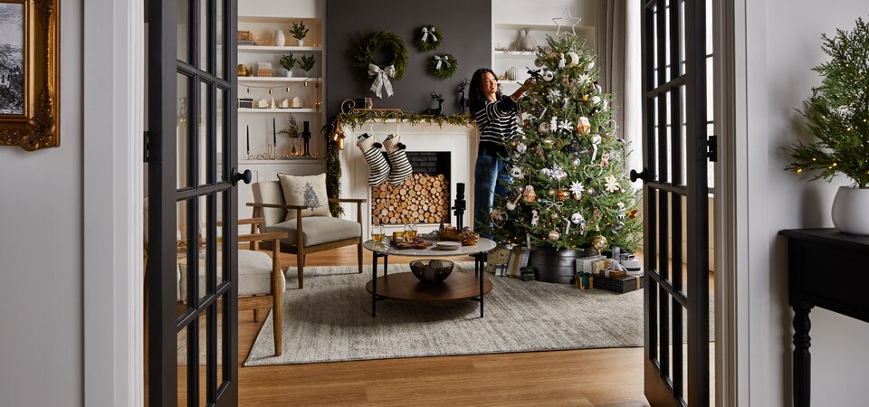 A woman in a living room decorating a tree with CANVAS Night Before Christmas decorations. 