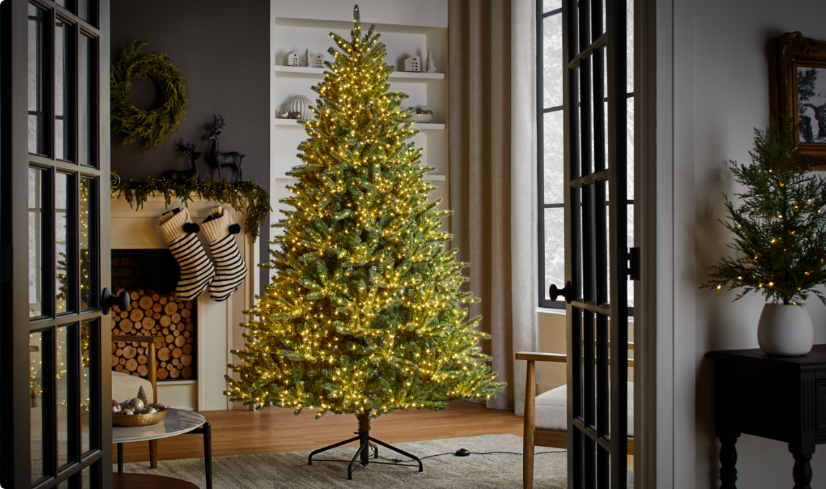 Un arbre scintillant NOMA Taylor avec des lumières chaudes dorées dans un salon. 