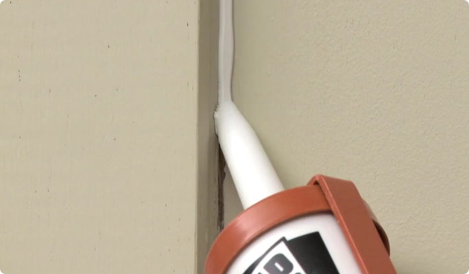 A tube of calking being applies to an interior wall.