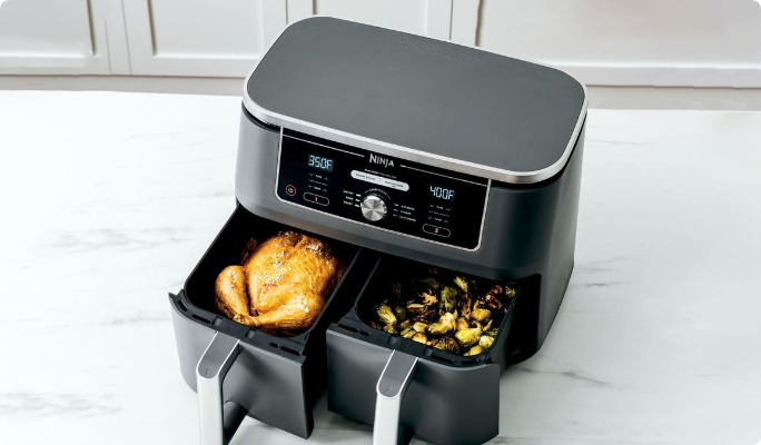 A freshly cooked chicken and brussels sprouts in the open baskets of a Ninja Foodi XL Dual Zone Air Fryer.