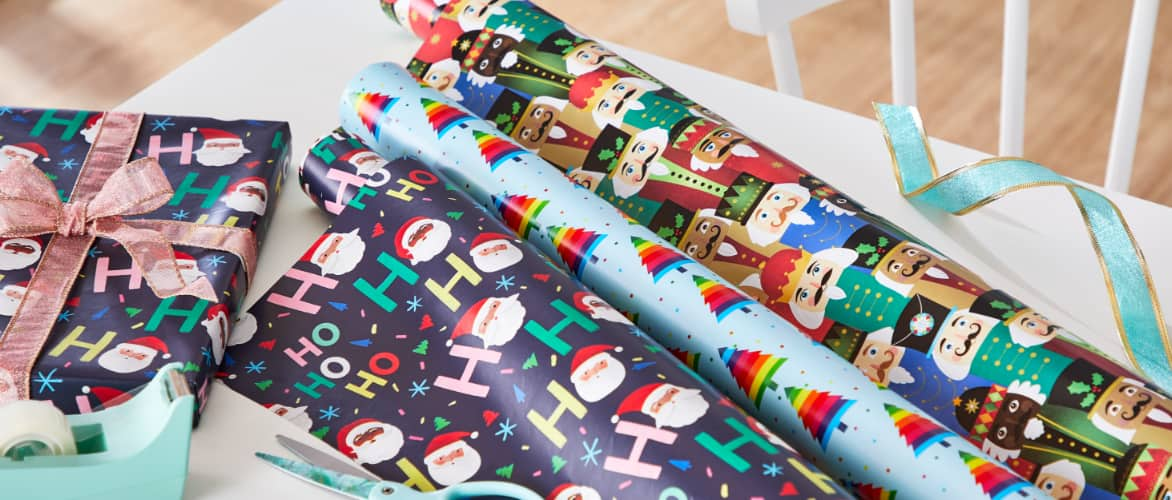 Rolls of CANVAS Merry Mingle wrapping paper and accessories on a table. 