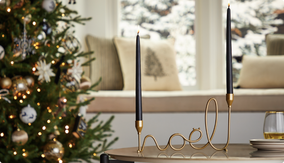 A brass CANVAS Noel taper candle holder on a table in a living room.