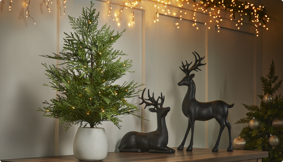 A CANVAS Pre-Lit Tabletop Potted Tree and deer figurines on a table. 