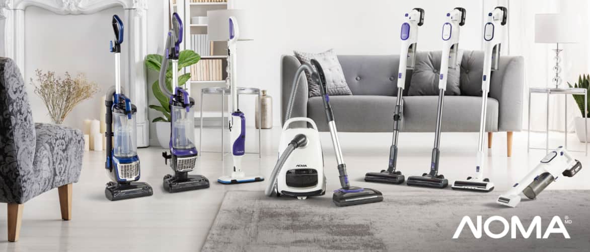 An assortment of eight styles and sizes of NOMA vacuums in a living room. 