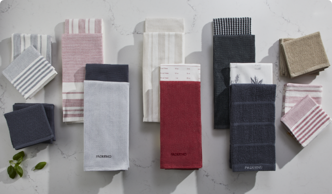 An assortment of PADERNO kitchen and dish towels and cloths on a marble countertop.