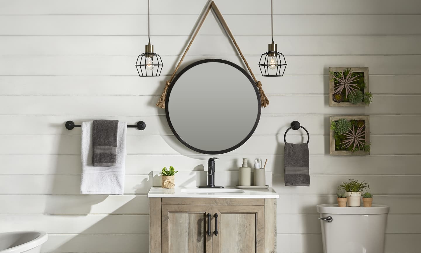A circular mirror hangs on the wall above a vanity in a rustic-look bathroom.