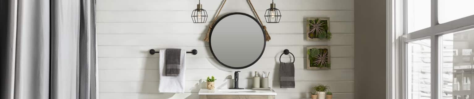 A circular mirror hangs on the wall above a vanity in a rustic-look bathroom.