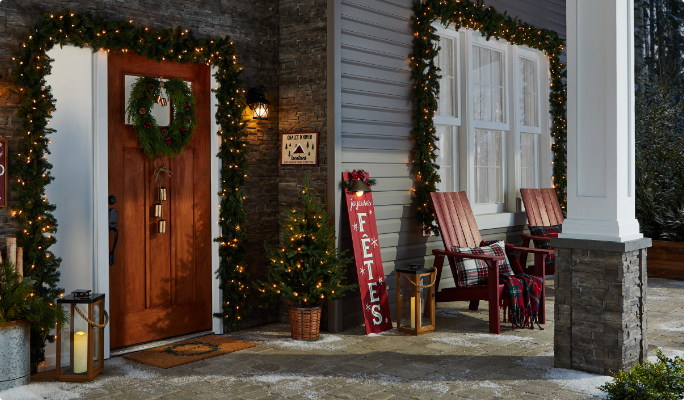 Un porche avant décoré avec des guirlandes de Noël, des arbres en pot et des décorations CANVAS.