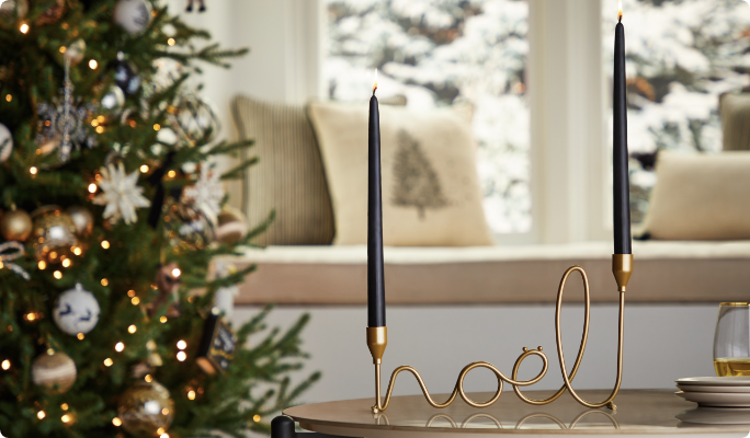 A brass CANVAS Noel taper candle holder on a table in a living room.