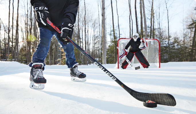 Two kids playing hockey on a frozen pond with Bauer and CCM hockey equipment. 