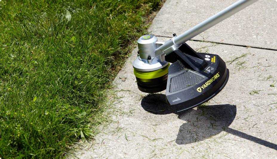 A Yardworks 48V Direct Drive Trimmer trimming grass along the edge of a sidewalk.