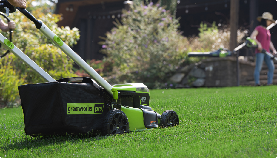 An adult pushing a Greenworks 60V Self Propelled Mower on a lawn.