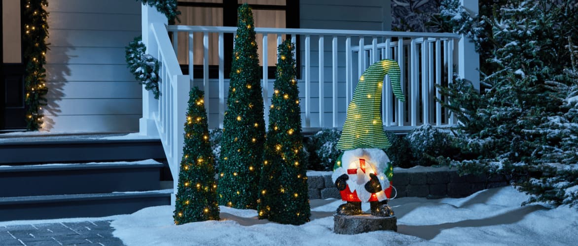 A CANVAS LED Whimsical Gnome and three Twinkling Topiary trees in a snowy front yard.