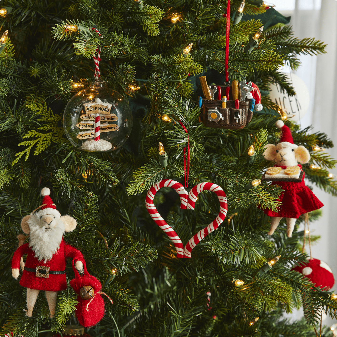 Assortiment de décorations CANVAS L'atelier du Père Noël suspendues à un arbre de Noël.