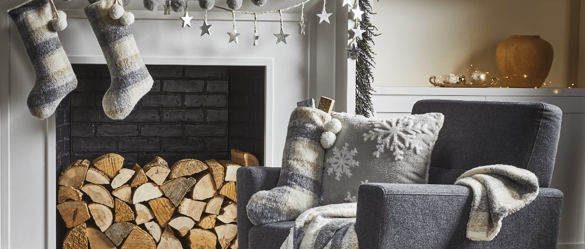 A chair with CANVAS Silver Frost cushions, stocking and throw blanket near a fireplace. 