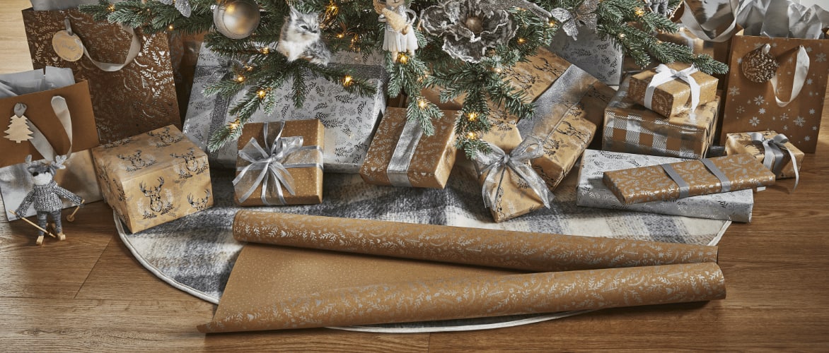 A roll of CANVAS Silver Frost wrapping paper and assorted wrapped gifts under a tree. 