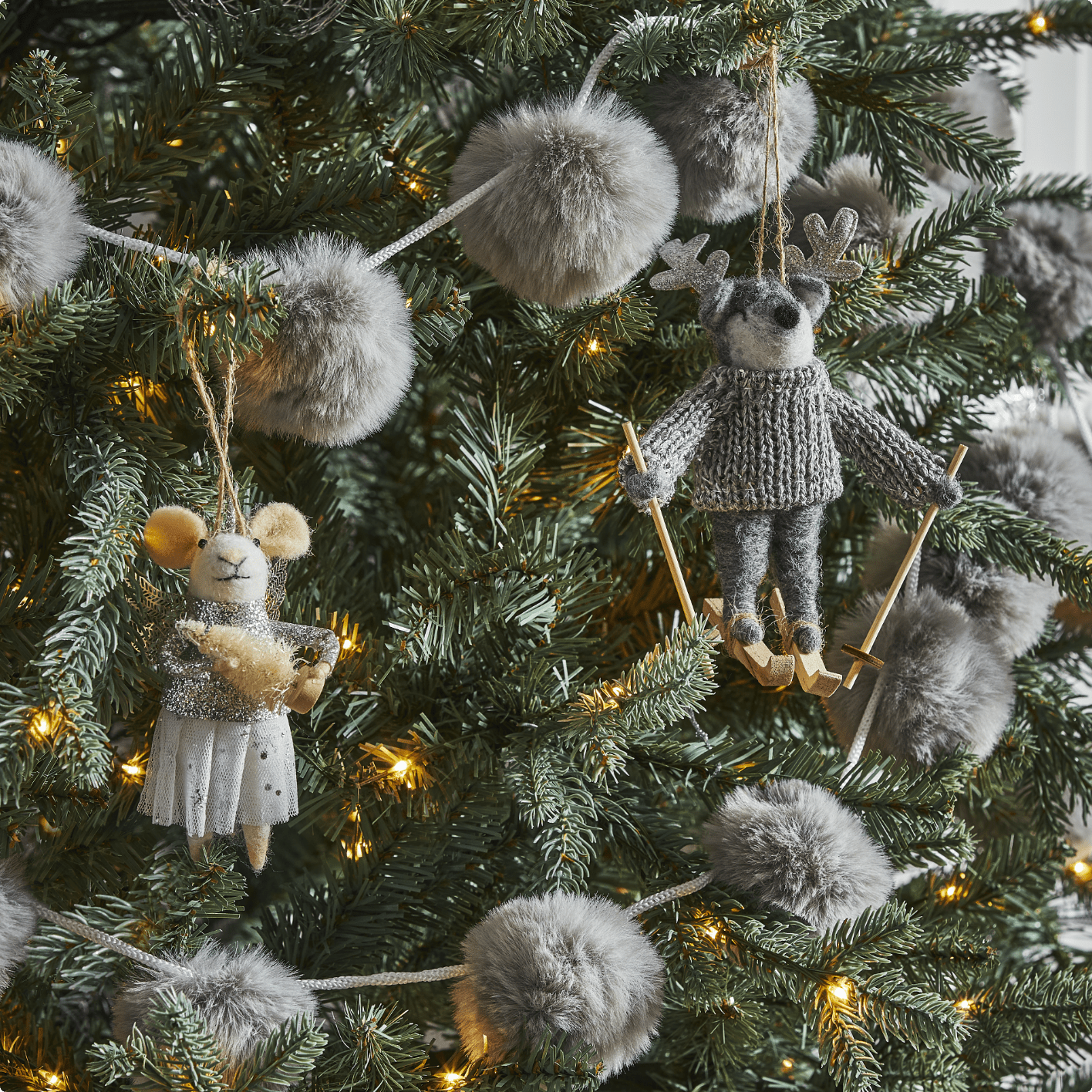 CANVAS Silver Fur Pom Pom Garland, a Unicorn Mouse ornament and Skiing Reindeer ornament on a tree. 