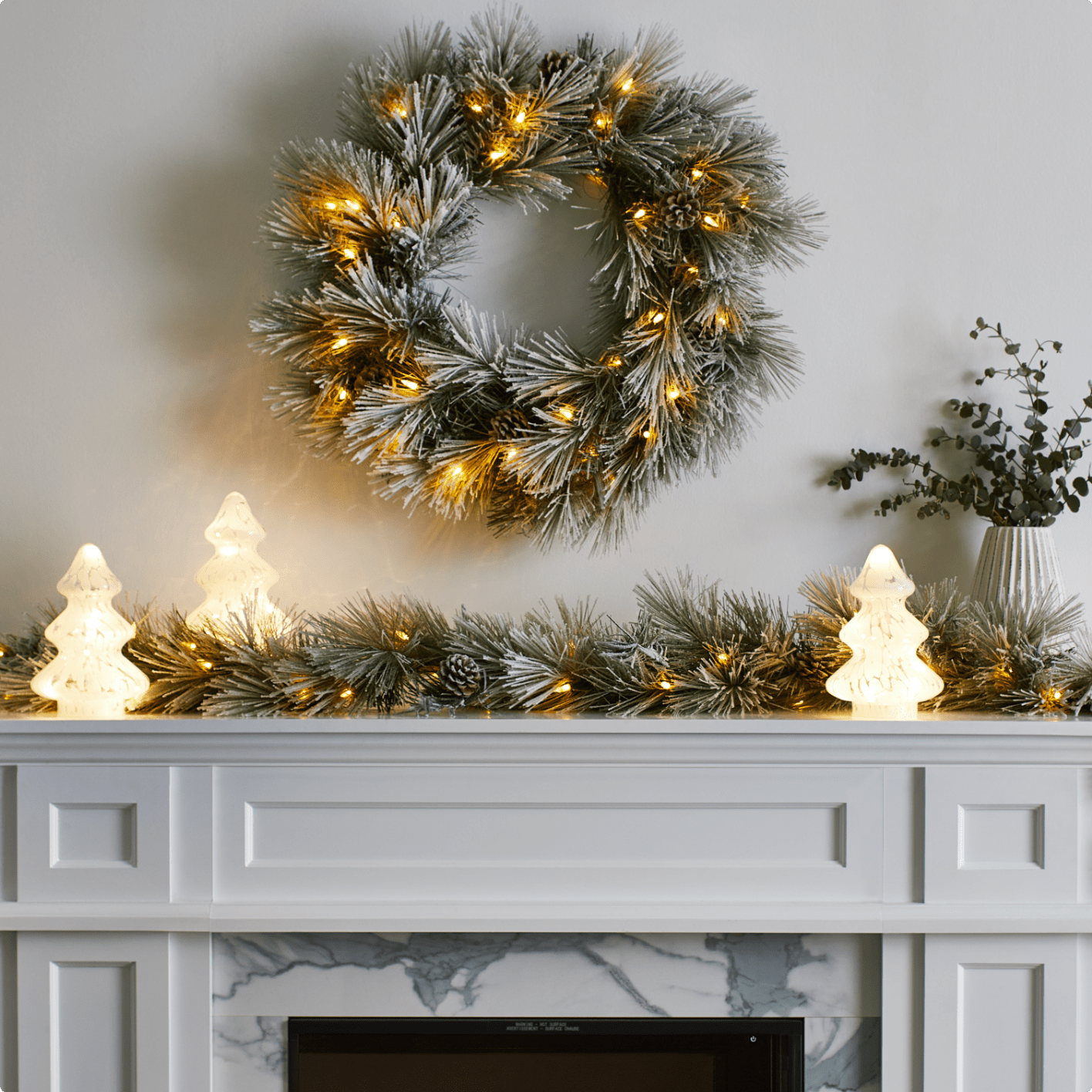 A mantle decorated with CANVAS Charlotte pre-lit garland and wreath and glass pre-lit trees. 