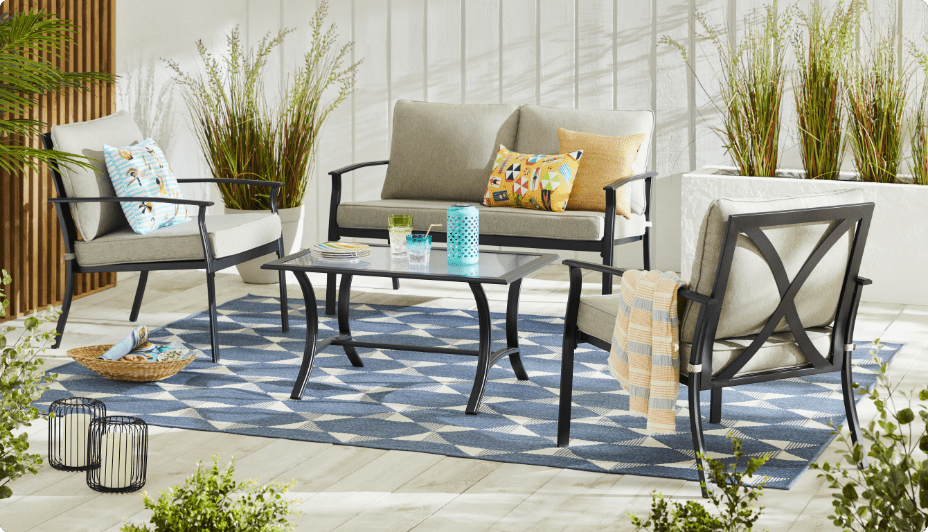 The 4-pc For Living Avenue Conversation Set on top of a patio rug surrounded by plants on a sunny day.