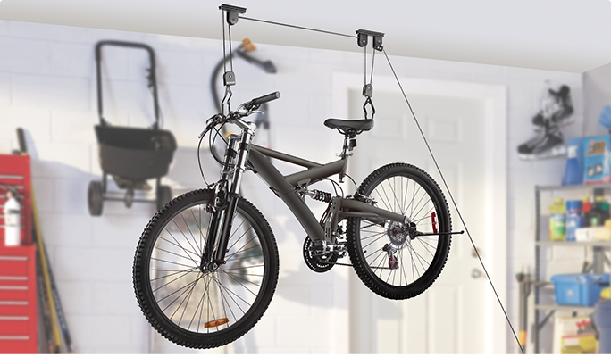 A black bicycle hangs from a ceiling mount pulley system in a garage.
