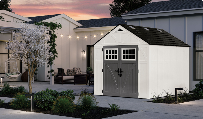 A white Suncast Tremont Storage Shed in a backyard at dusk. 