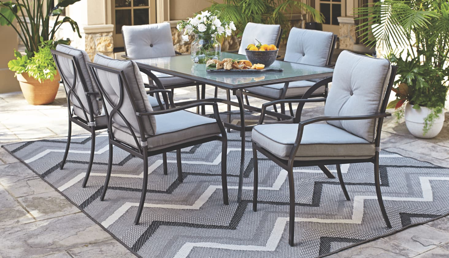 A For Living Bluebay Glass Table with 6 Bluebay Padded Dining Chairs and an outdoor rug on a patio.