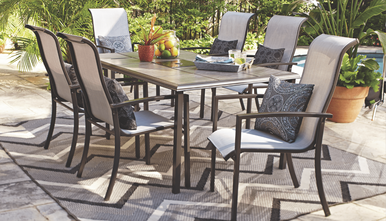 A For Living Bluebay Steel Table with 6 Bluebay Sling Dining Chairs and an outdoor rug on a patio.