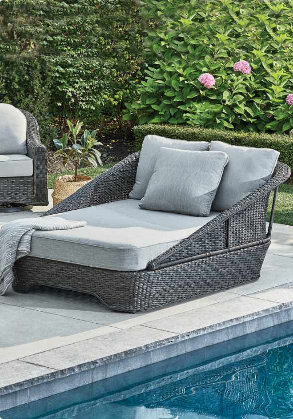  A wicker CANVAS Summerhill Daybed with grey cushions next to a pool.