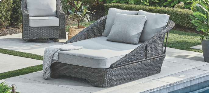  A wicker CANVAS Summerhill Daybed with grey cushions next to a pool.