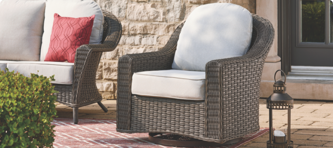 A wicker CANVAS Summerhill Swivel Glider Armchair with white cushions on a patio.