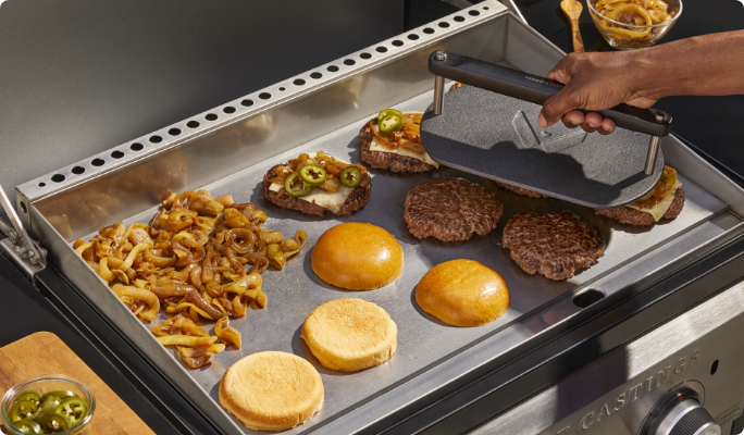 An overhead shot of someone pressing meat on the griddle.