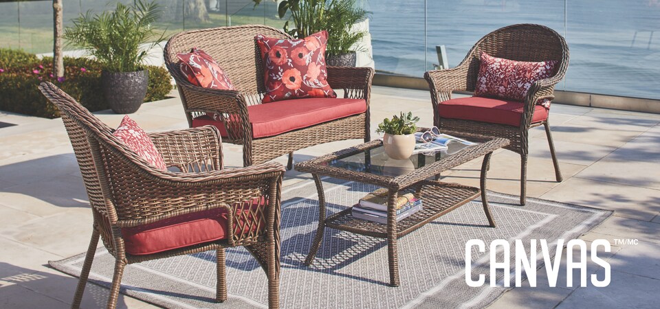 A CANVAS Canterbury Coffee Table, Loveseat and two Armchairs styled with red cushions, on top of a grey carpet on a patio by a lake.