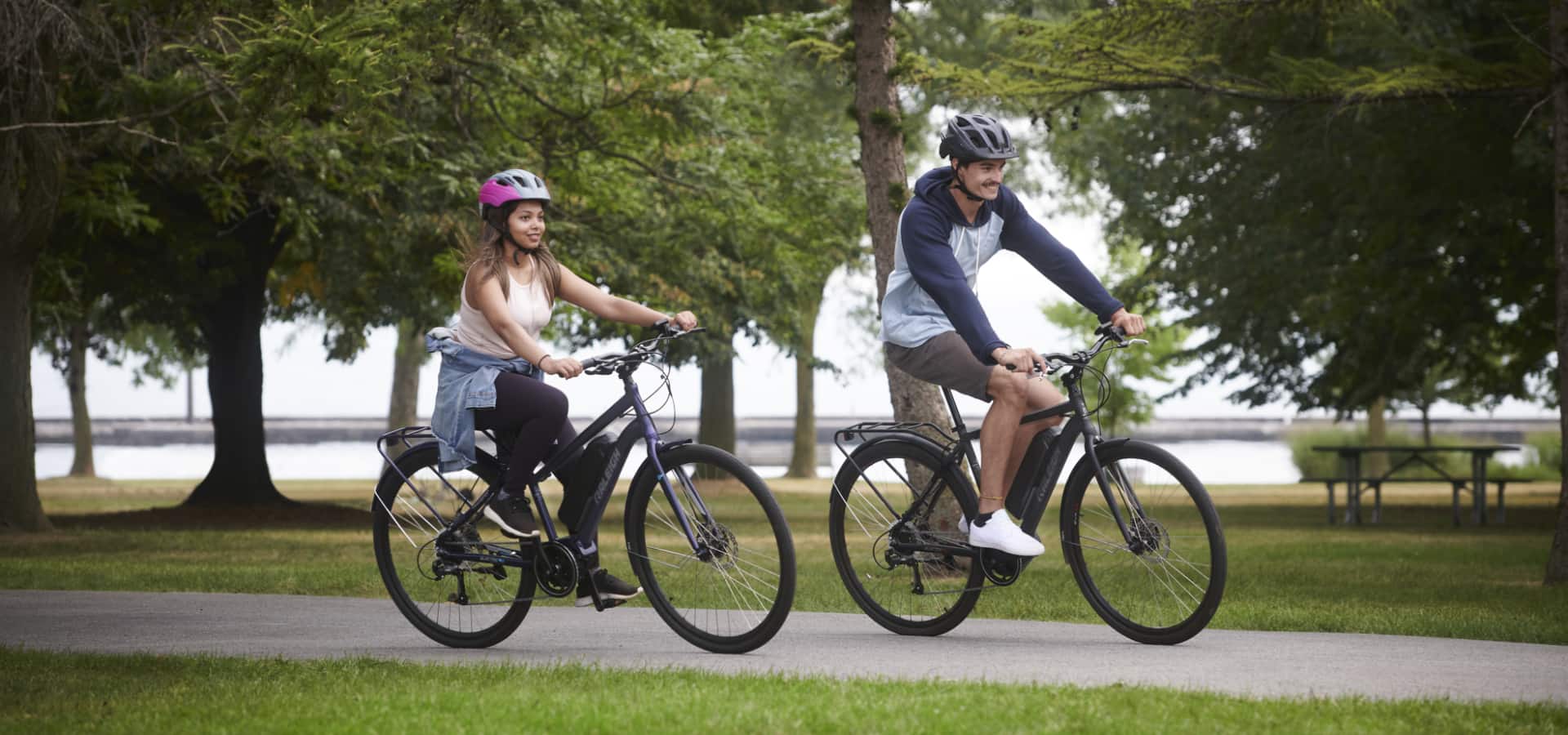 Two adults riding Raleigh Getaway Electric Bicycles on a park bike trail.