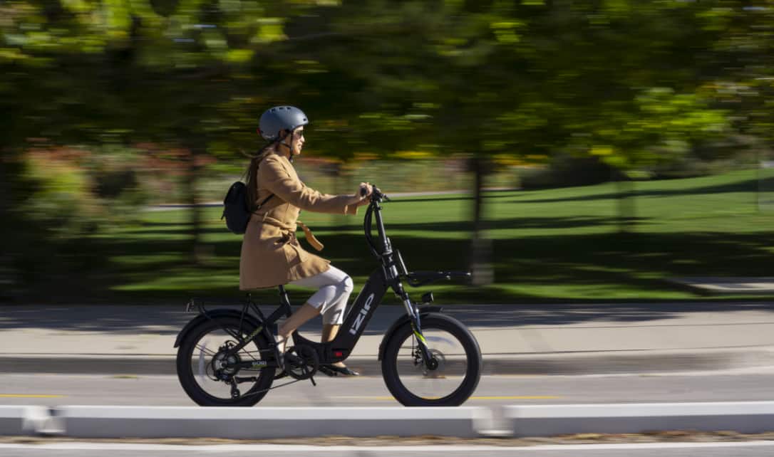 A woman riding an iZip Electric Bike on a city street.
