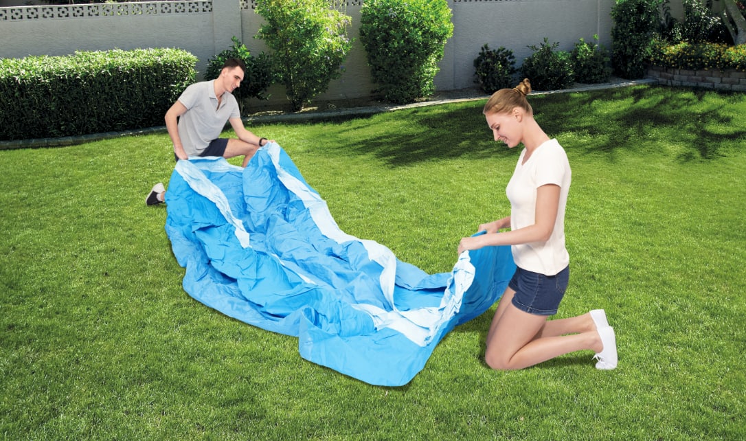 Two adults laying a deflated fast set pool in a backyard. 