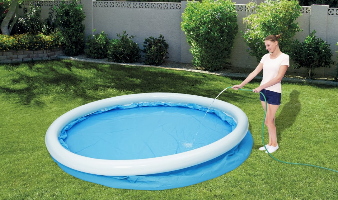 A woman filling a fast set pool with water using a garden hose. 