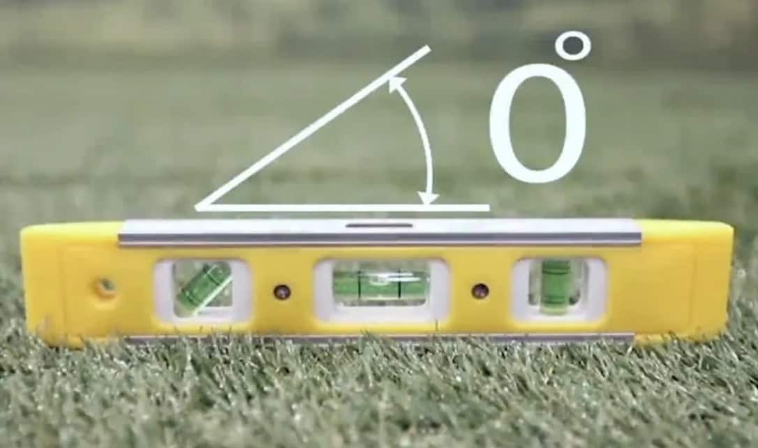 A small yellow level tool measuring a grassy ground. 