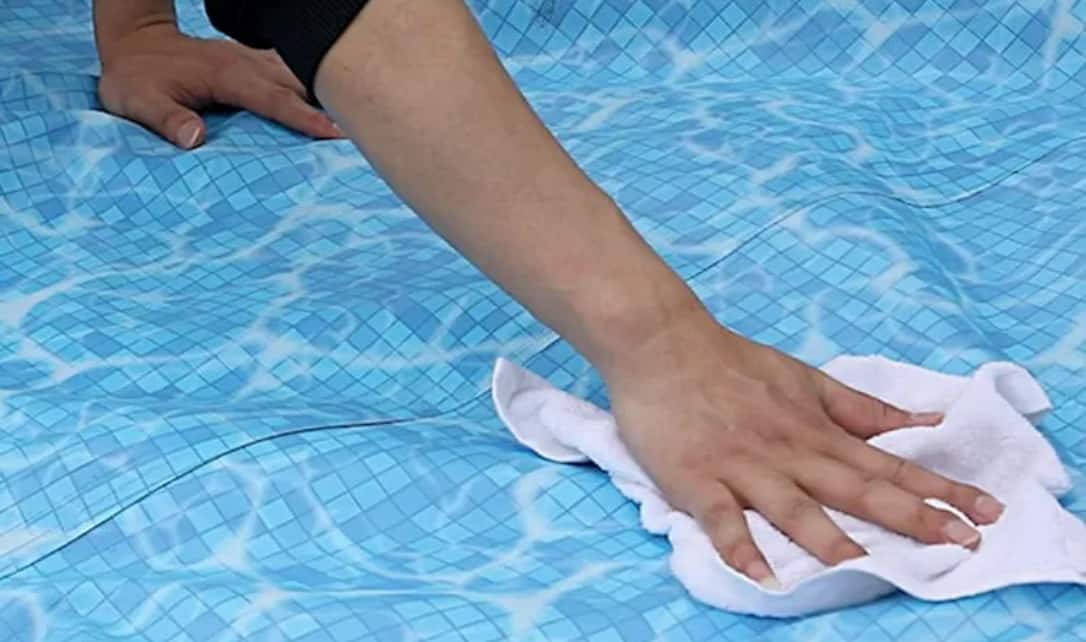An adult wiping the liner of a disassembled pool with a cloth.