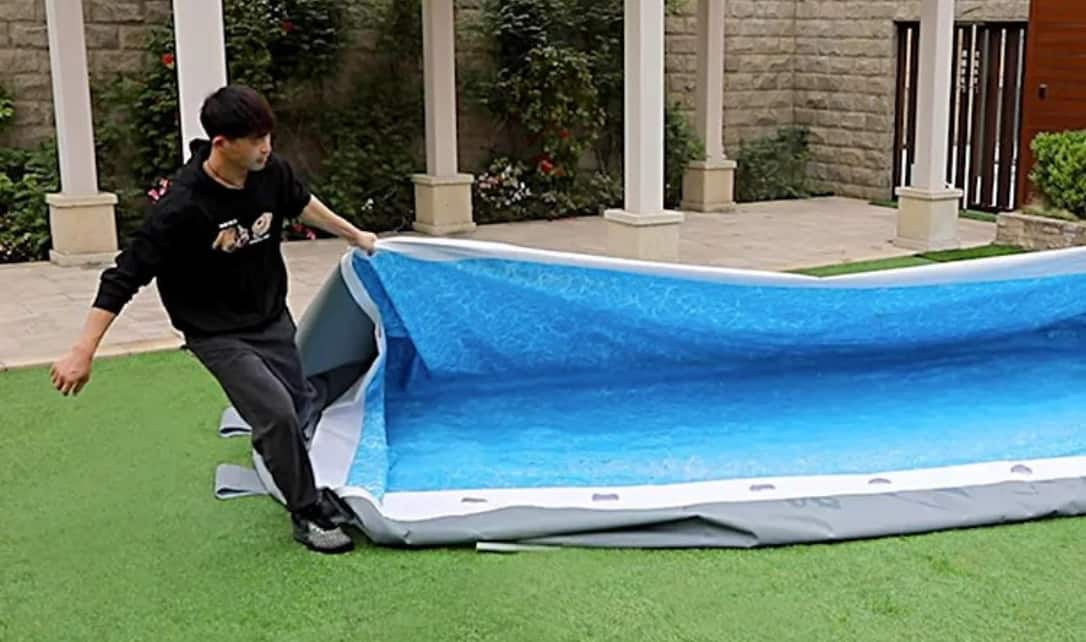 An adult folding the liner of a disassembled steel frame pool. 