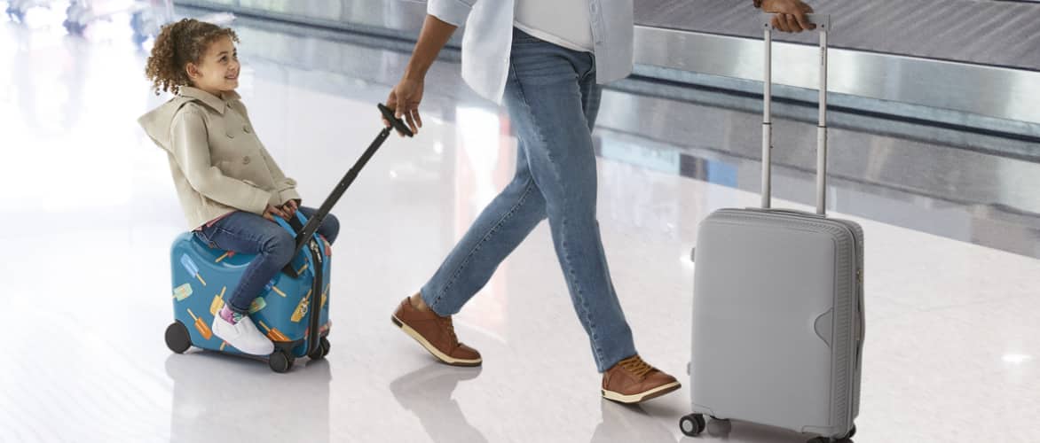 Un enfant monte sur une valise à roulettes tandis qu'un adulte la tire dans un aéroport.