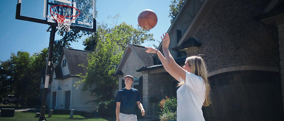 Two teenagers playing basketball in front of their home.