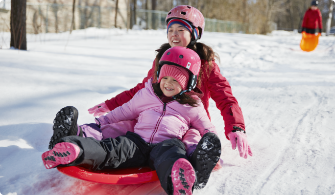 Two children sliding down a snowy hill on a sled.