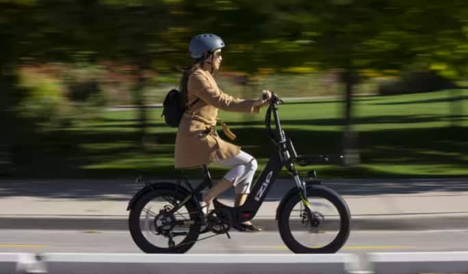 A woman riding an iZip Electric bike on a city street.