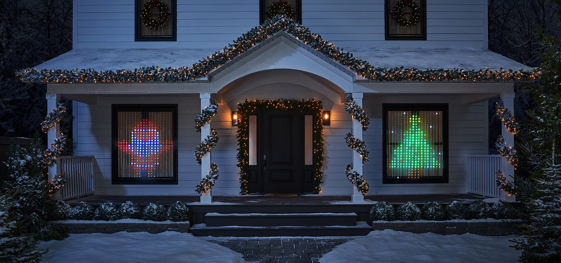 The front of a house decorated with lighted garland, wreaths and Christmas-themed curtain lights in the two front windows.