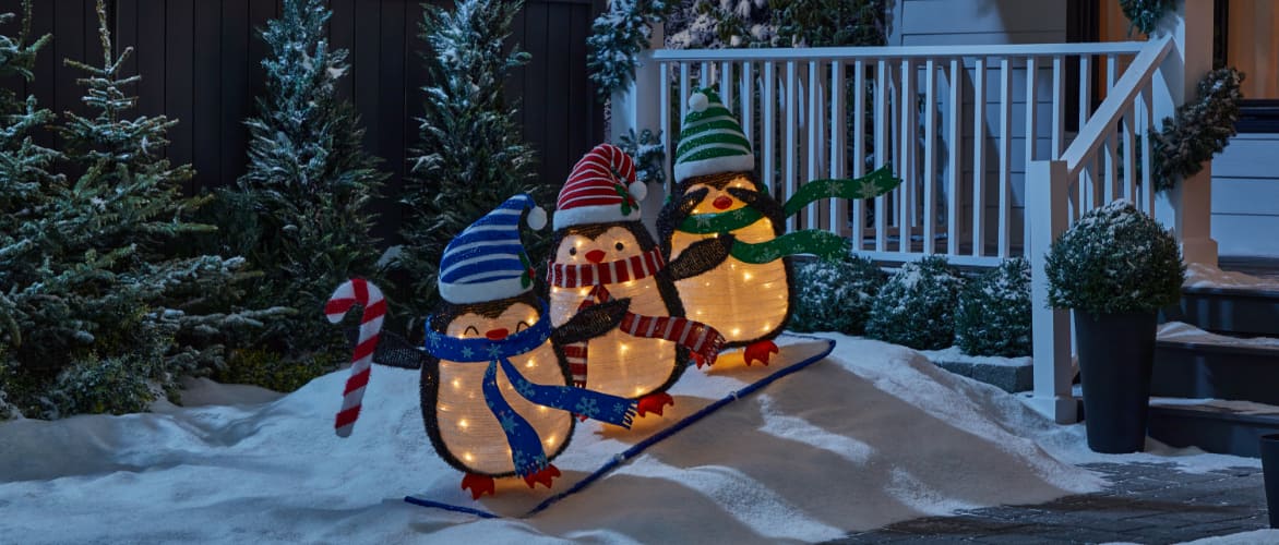 Three pre-lit CANVAS Skiing Collapsible Penguin decorations in a snowy yard.