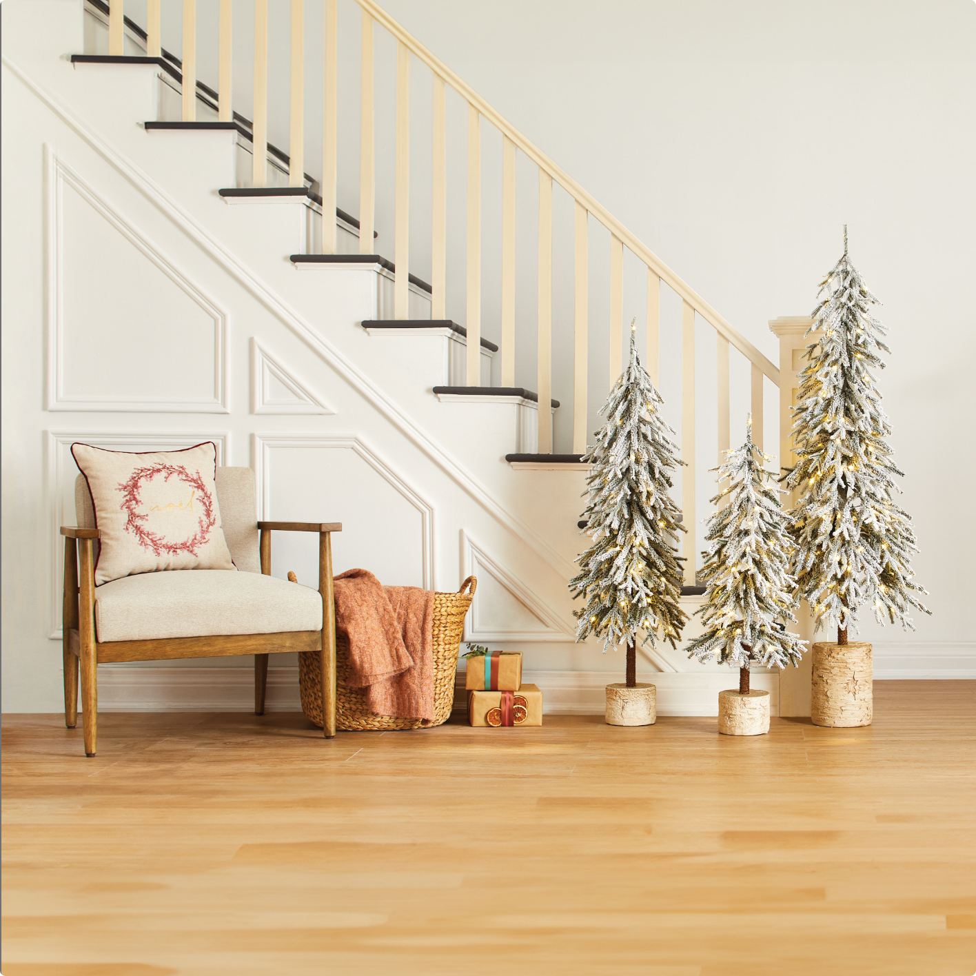 Three CANVAS Flocked trees and a chair with a Christmas cushion next to a stairway.