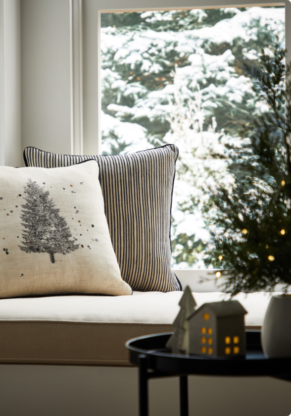 A window seat with CANVAS Christmas cushions and decorations on a table. 