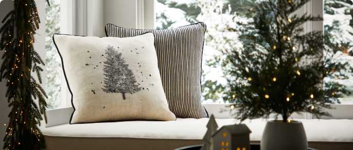 A window seat with CANVAS Christmas cushions and decorations on a table. 