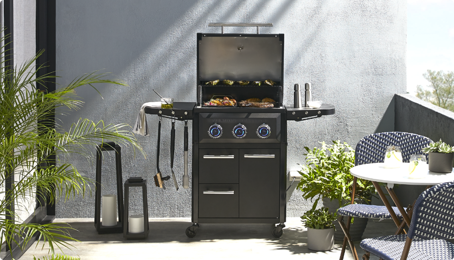 A Vermont Castings Ascent™ 3-Burner Electric Balcony Grill next to a small conversation set and plants on a balcony.